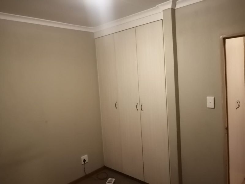A clean, empty bedroom featuring neutral-toned walls, coving, and built-in cupboards, providing a versatile space ready for personalization.