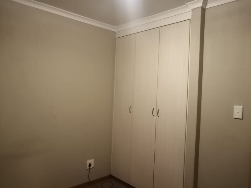 A clean, empty bedroom featuring neutral wall paint and functional built-in cupboards with light wood-grain finish.