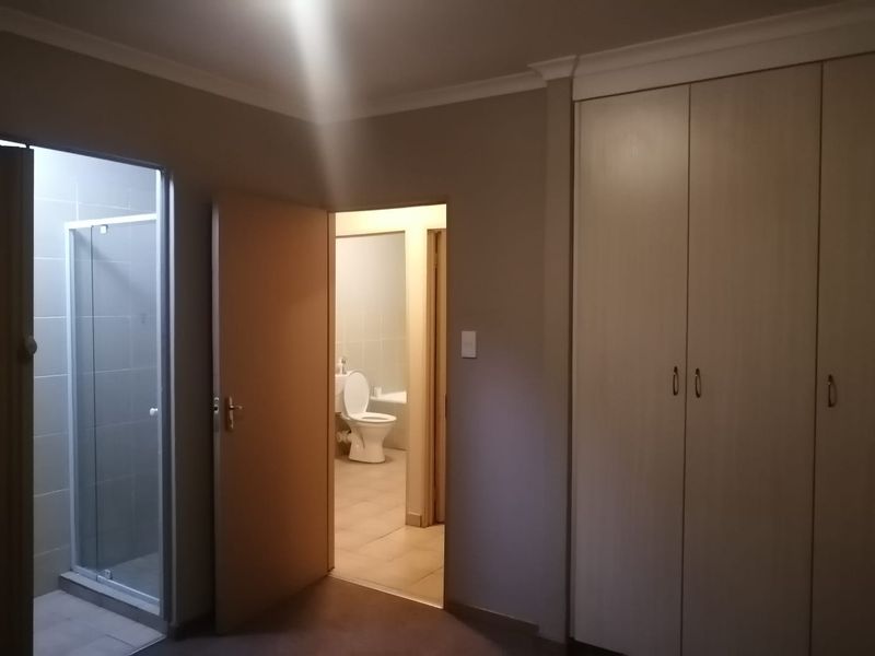 A bedroom featuring built-in cupboards and an en-suite bathroom with a shower and toilet, finished with neutral wall tones and tiled flooring.