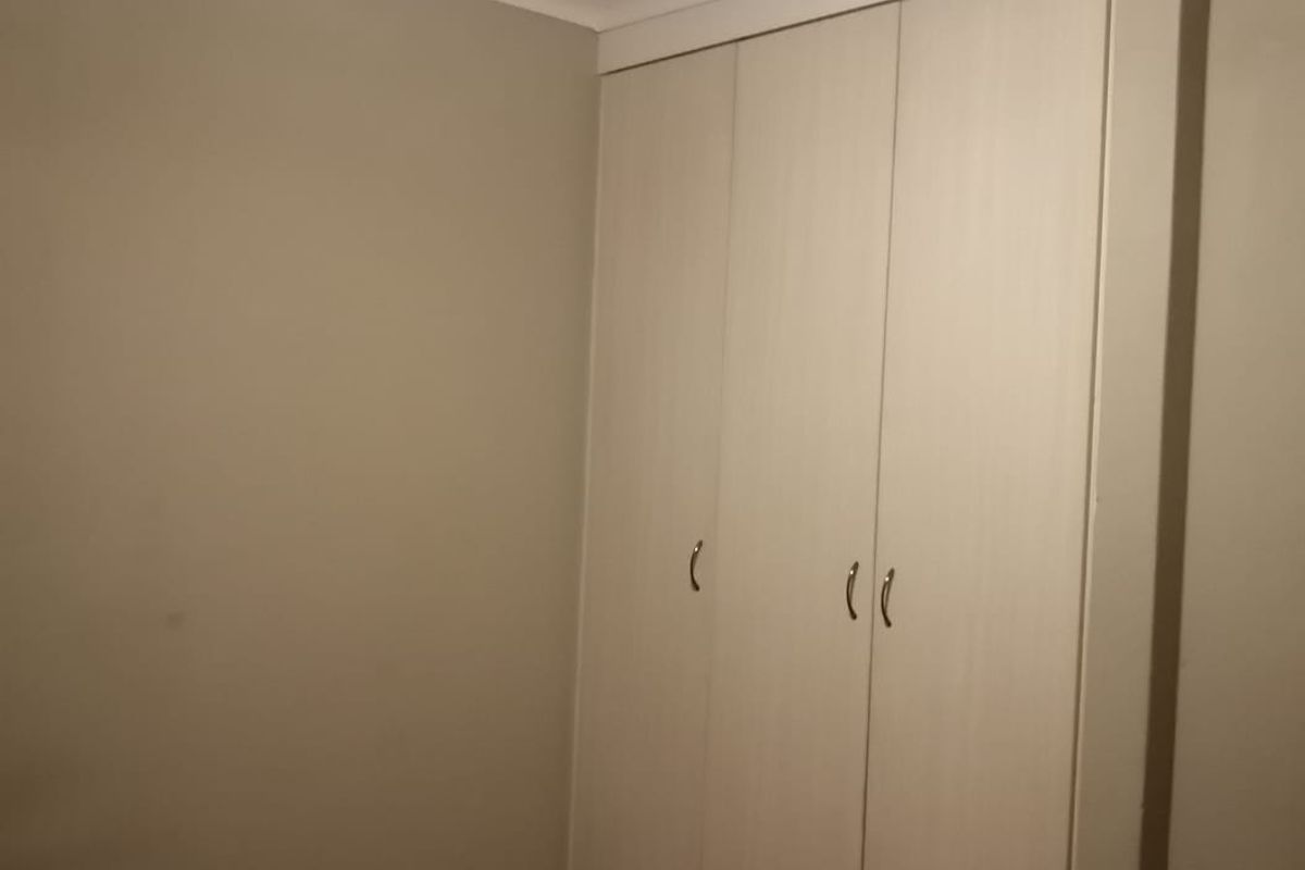 A clean, empty bedroom featuring neutral wall paint, carpeted flooring, and a functional built-in wardrobe with light wood-finish doors.