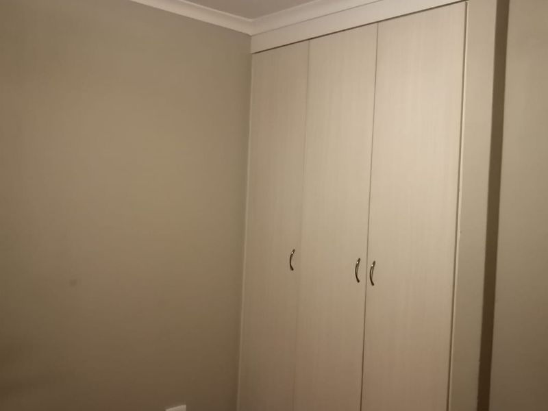 A clean, empty bedroom featuring neutral wall paint, carpeted flooring, and a functional built-in wardrobe with light wood-finish doors.