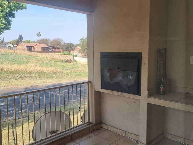 Covered balcony featuring a built-in braai, tiled flooring, and a metal balustrade, offering an open view of the surrounding neighbourhood.