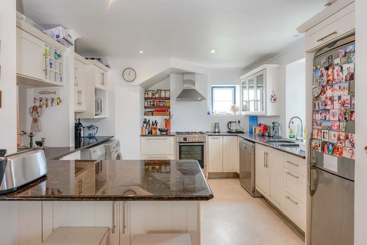 A well-appointed kitchen featuring granite countertops, shaker-style cabinetry, and integrated stainless steel appliances, including an oven, extractor fan, and dishwasher.