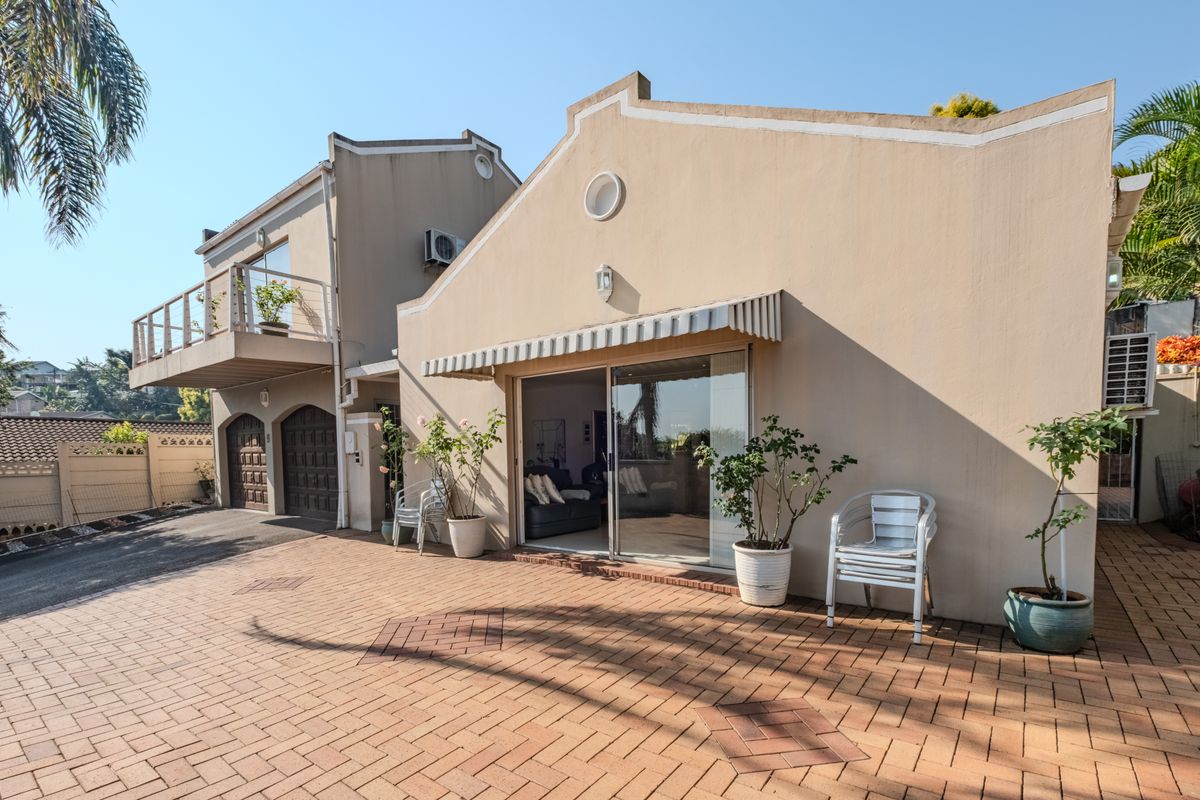 Rear exterior view of the property featuring a paved patio area, sliding glass doors, a balcony, and integrated garage access.