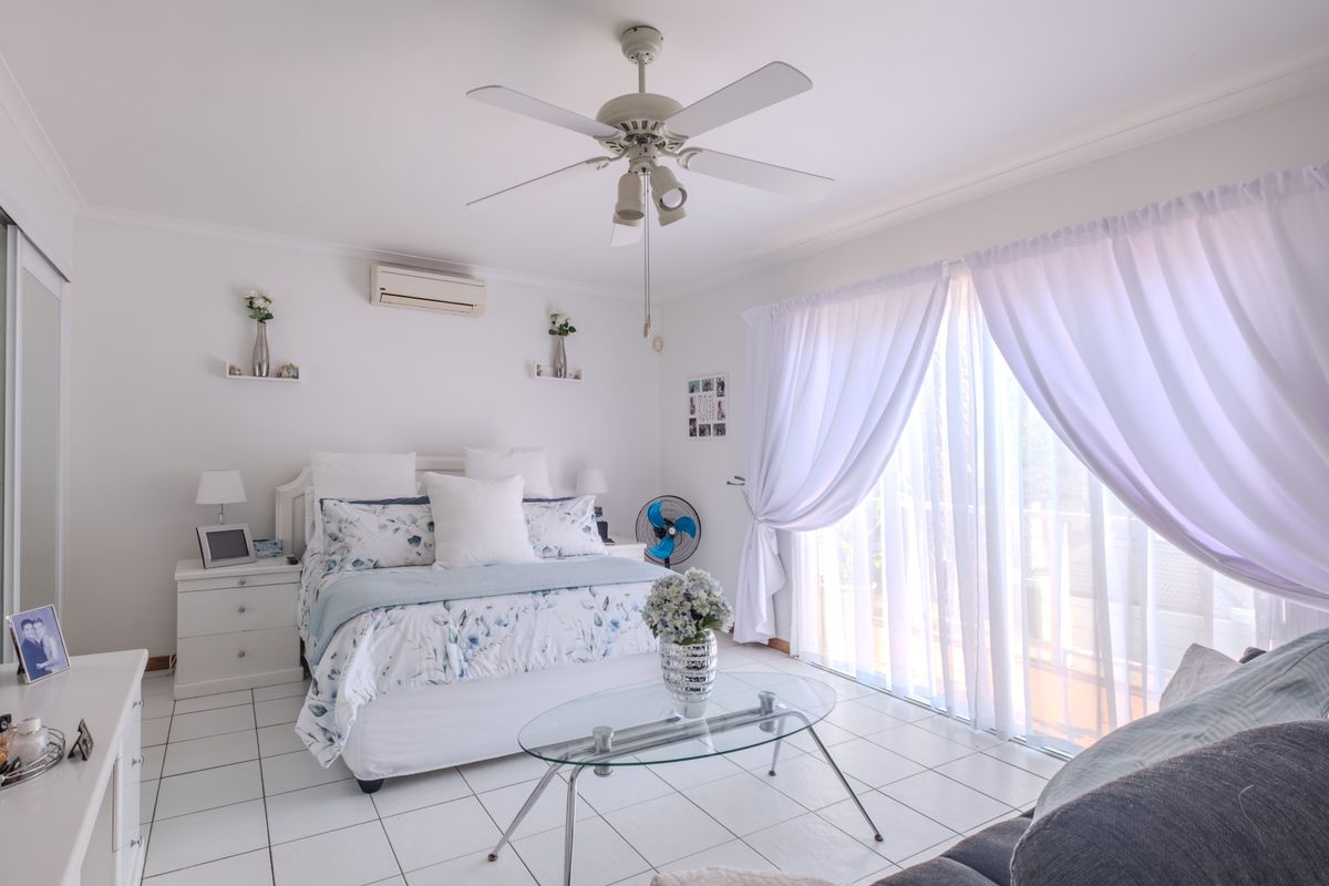 A bright and well-maintained bedroom featuring tiled flooring, a ceiling fan, split-system air conditioning, and sliding glass doors providing access to the outdoors.