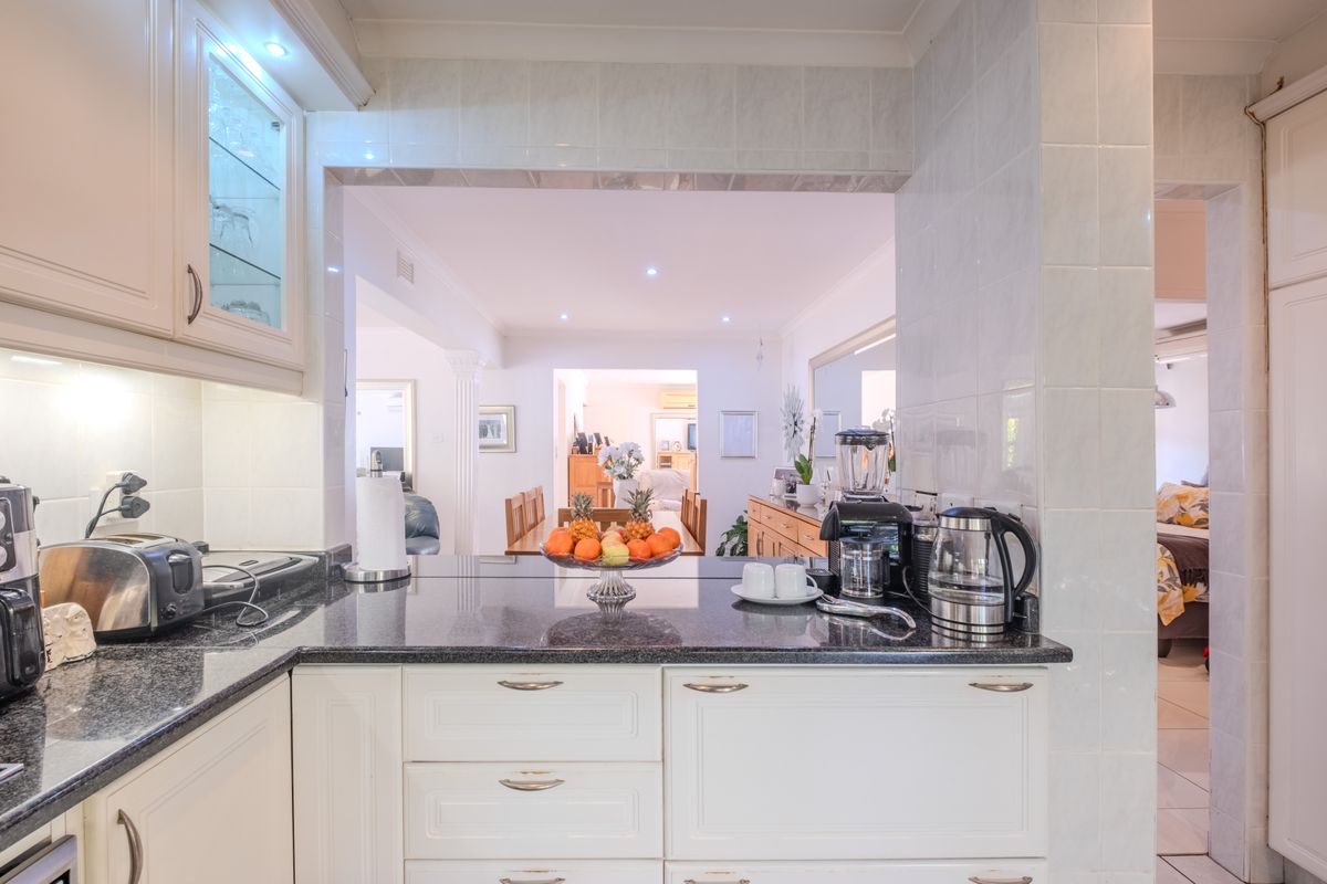 A well-maintained kitchen featuring granite countertops, shaker-style cabinetry, and a tiled backsplash, with an open-plan view into the adjacent dining and living areas.