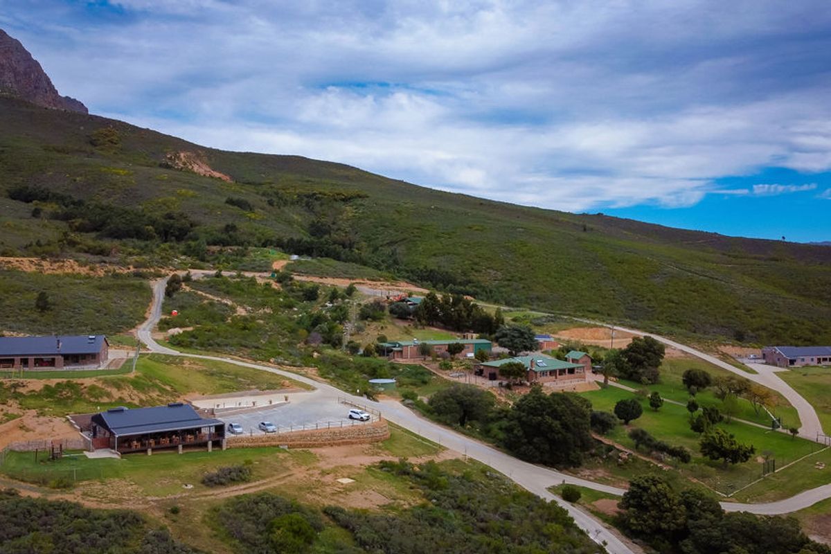 Aerial view of a farm estate featuring multiple buildings, paved access roads, parking areas, and expansive mountain landscape surroundings.