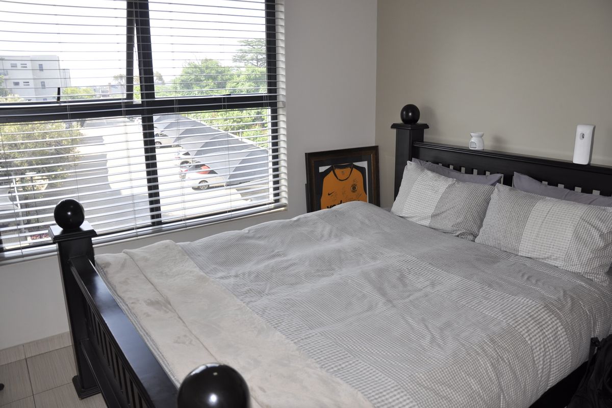 A well-lit bedroom featuring large windows with fitted blinds, neutral wall tones, and tiled flooring, offering a comfortable and functional living space.
