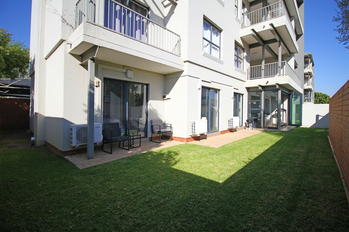 A rear view of the apartment building featuring a private garden, paved patio area, and multiple sliding glass doors leading to the interior.