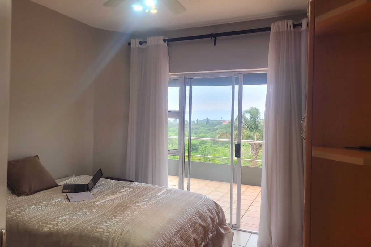 A bedroom featuring a ceiling fan and sliding glass doors that open onto a private balcony with scenic views.