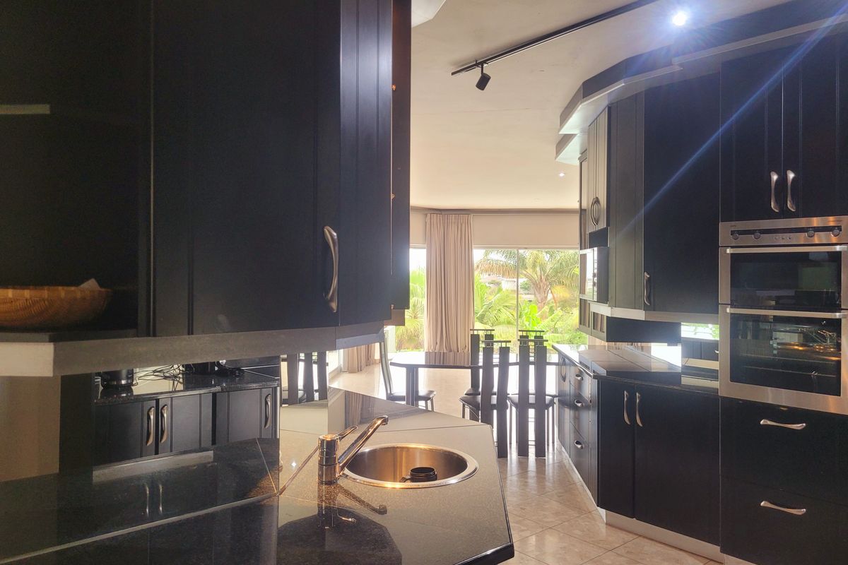 Modern kitchen featuring dark cabinetry, granite countertops, integrated oven, and tiled flooring, flowing into an open-plan living area with garden views.