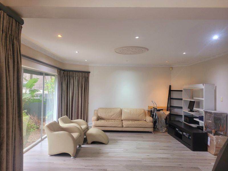 Spacious living room featuring modern laminate flooring, recessed downlighting, decorative ceiling rose, and large sliding glass doors providing access to the garden.