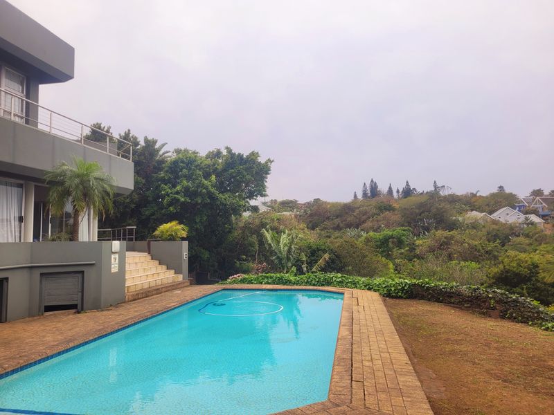 Outdoor pool area featuring a swimming pool, brick paved surround, and concrete stairs leading to a multi-level home with scenic garden views.