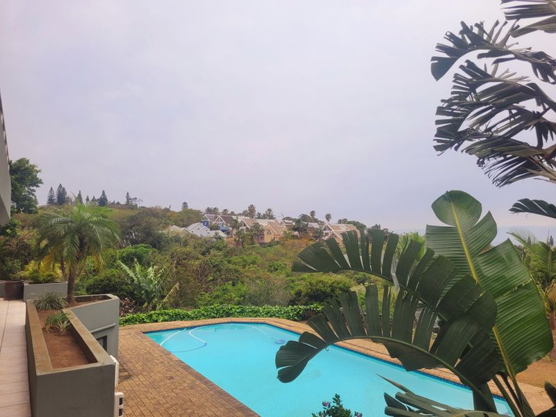 Outdoor pool area featuring a swimming pool, brick paved surround, and built-in planters, set against a scenic landscape view.