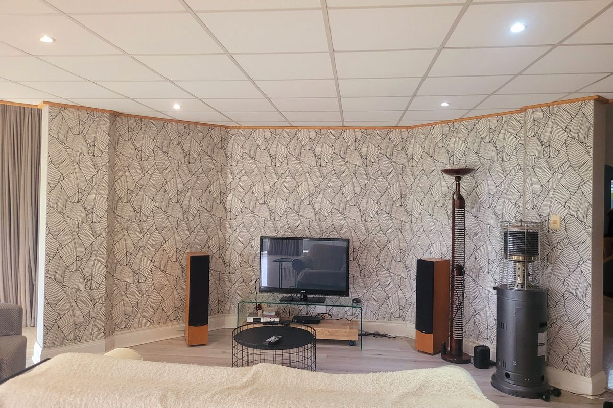 A living room featuring a curved wall with patterned wallpaper, recessed downlights, a suspended ceiling, and light-toned laminate flooring.