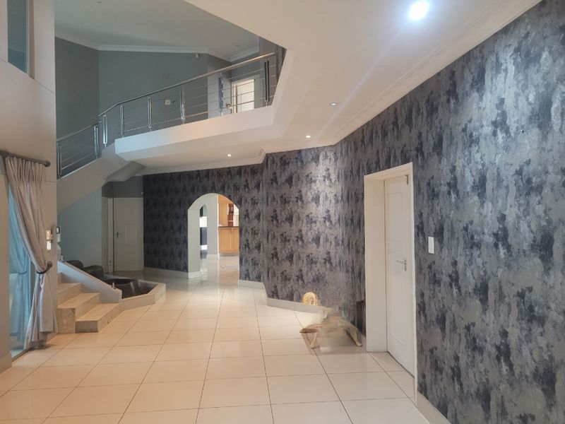 Spacious double-volume entrance hall featuring a modern staircase with stainless steel balustrades, tiled flooring, and decorative textured wallpaper.