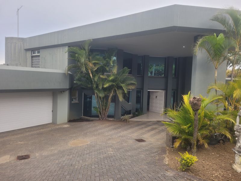 Modern architectural front elevation featuring a paved driveway, double garage, and a covered entrance with large glass windows.
