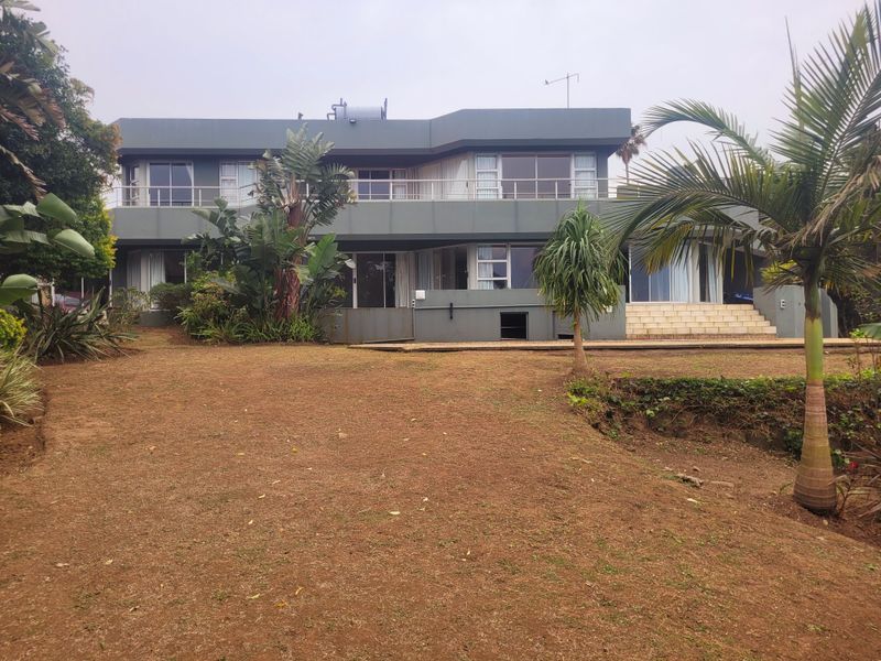 Rear view of a two-story house featuring a large balcony, sliding glass doors, and a spacious garden area.