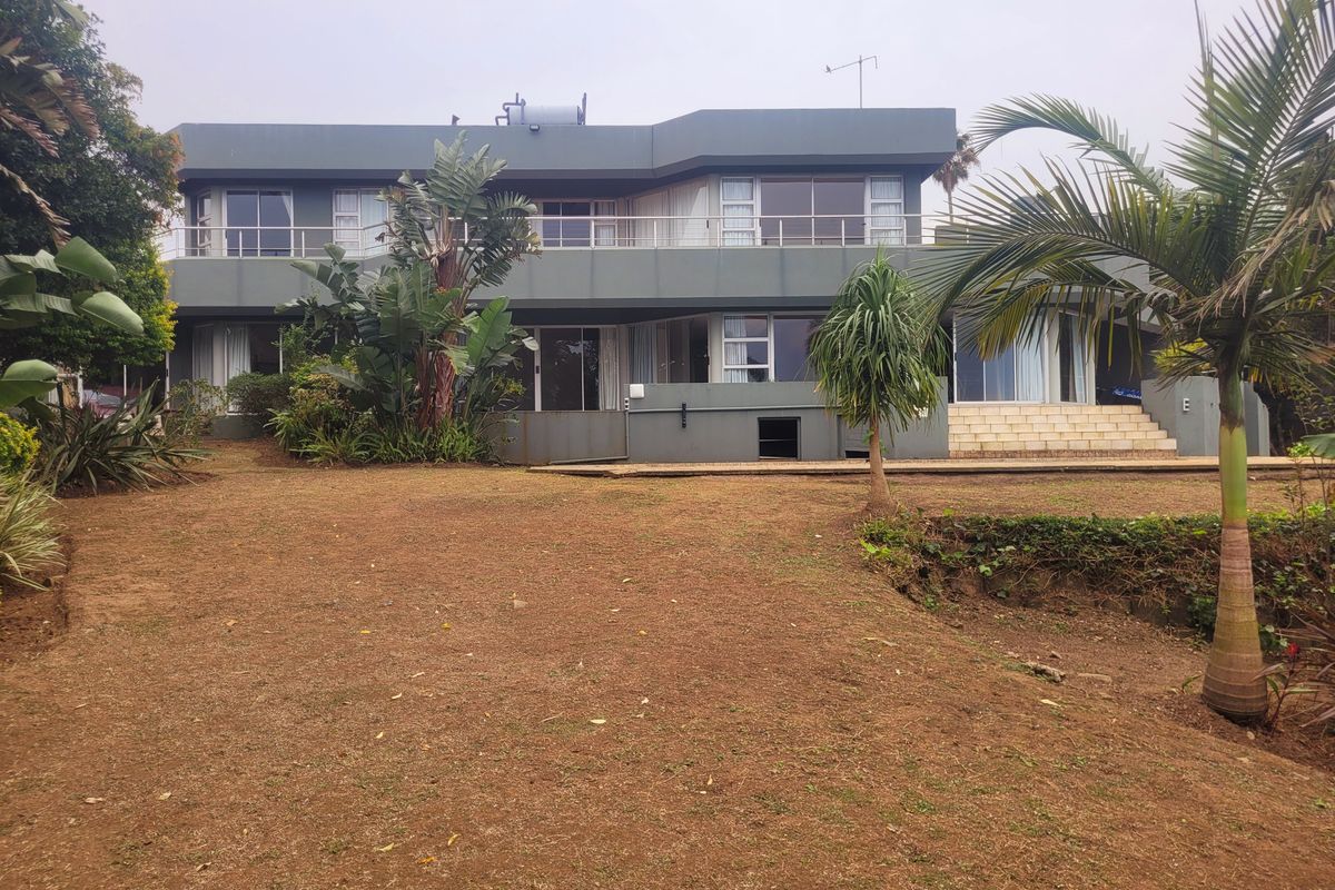 Rear view of a two-story house featuring a large balcony, sliding glass doors, and a spacious garden area.
