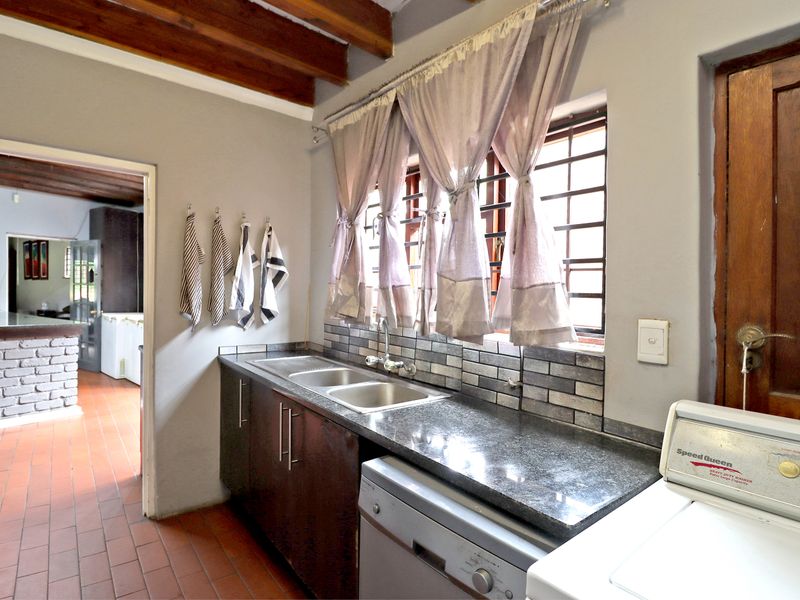 Functional laundry room featuring granite countertops, double stainless steel sink, tiled backsplash, and exposed timber ceiling beams.