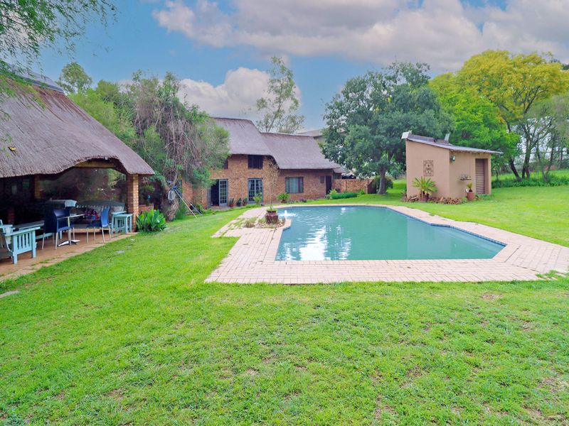 Spacious backyard featuring a swimming pool, a thatched roof lapa for outdoor entertaining, and a separate outbuilding set within a large garden.