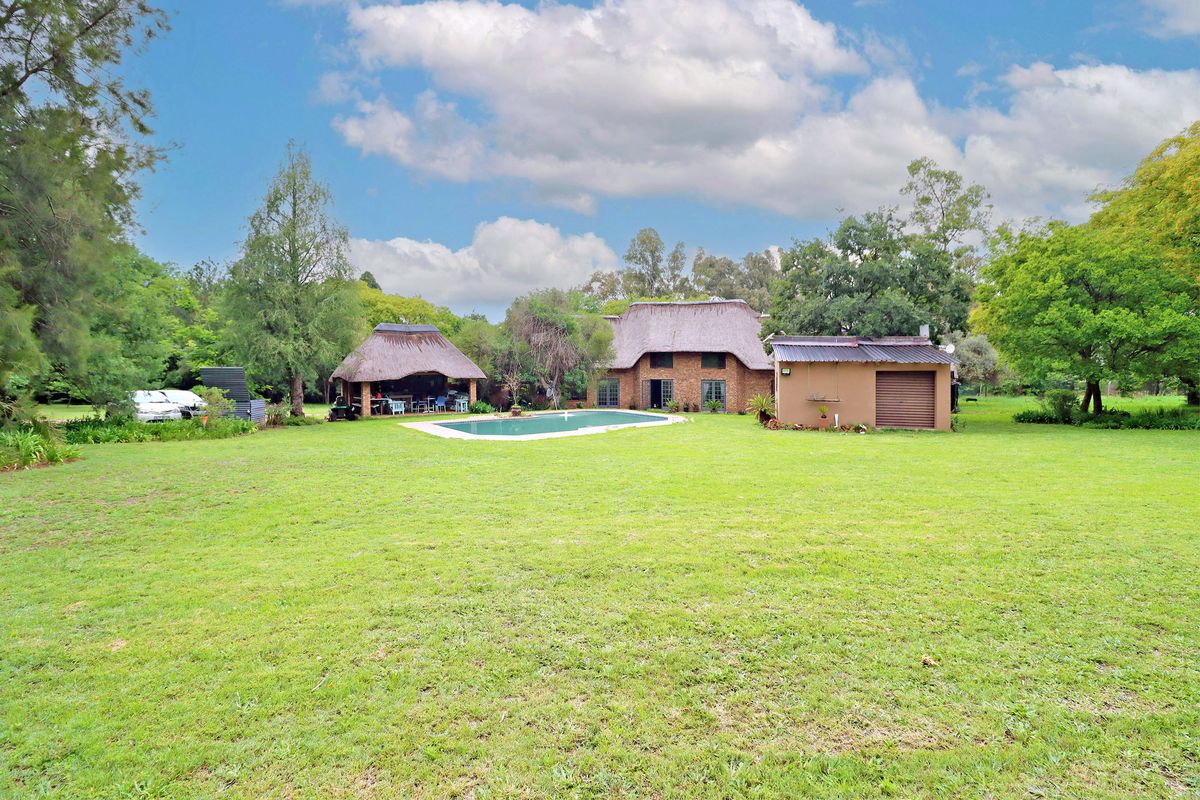 Spacious rear garden featuring a swimming pool, a thatched lapa entertainment area, and a detached garage set against the main thatched roof residence.