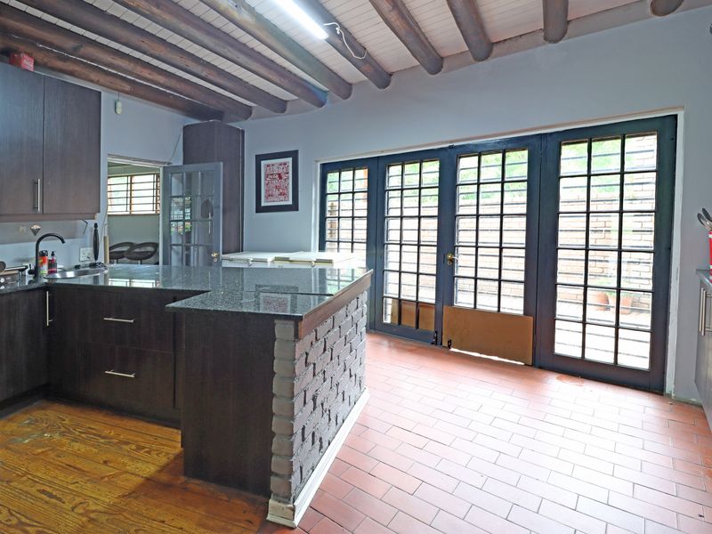 Spacious kitchen featuring dark cabinetry, granite countertops, a brick-based breakfast bar, exposed timber ceiling beams, and direct access to the outdoors via french doors.