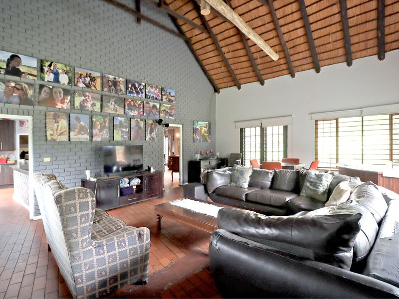 Spacious open-plan living area featuring a high vaulted thatched ceiling with exposed timber rafters, a textured brick feature wall, and terracotta tile flooring.