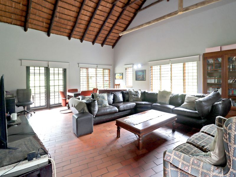 Spacious living room featuring a high vaulted thatched ceiling with exposed timber beams and traditional terracotta tile flooring, offering a rustic and airy atmosphere.