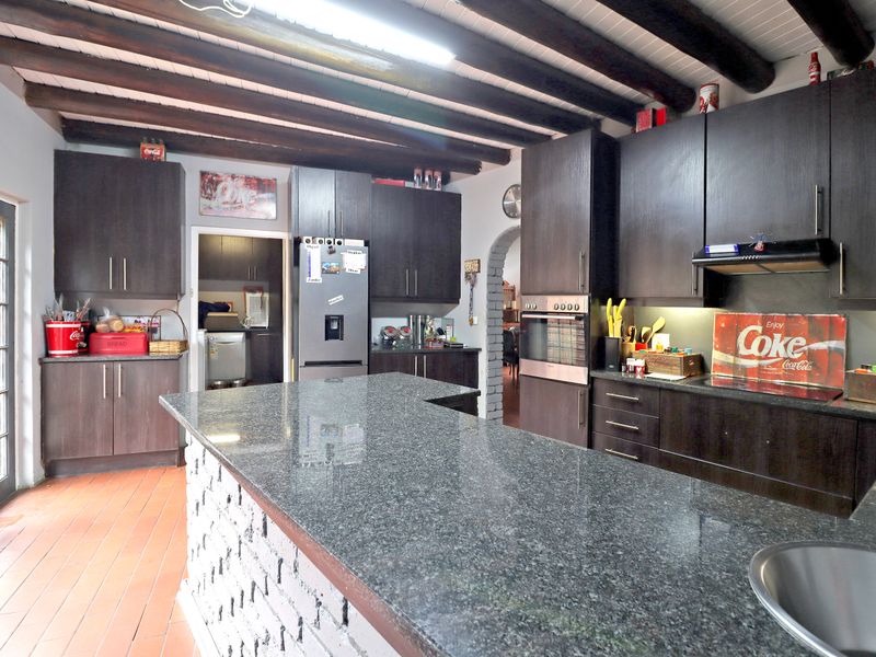 Spacious kitchen featuring dark cabinetry, granite countertops, a central island, and rustic exposed timber ceiling beams with terracotta flooring.