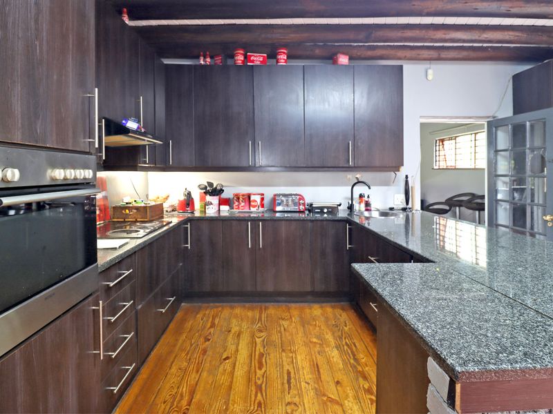 A well-appointed kitchen featuring dark wood cabinetry, granite countertops, built-in oven, and exposed timber ceiling beams, complemented by warm hardwood flooring.