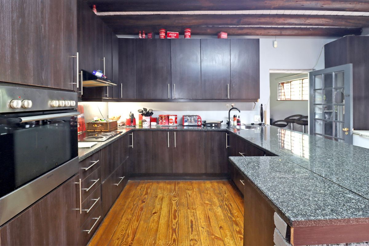 A well-appointed kitchen featuring dark wood cabinetry, granite countertops, built-in oven, and exposed timber ceiling beams, complemented by warm hardwood flooring.