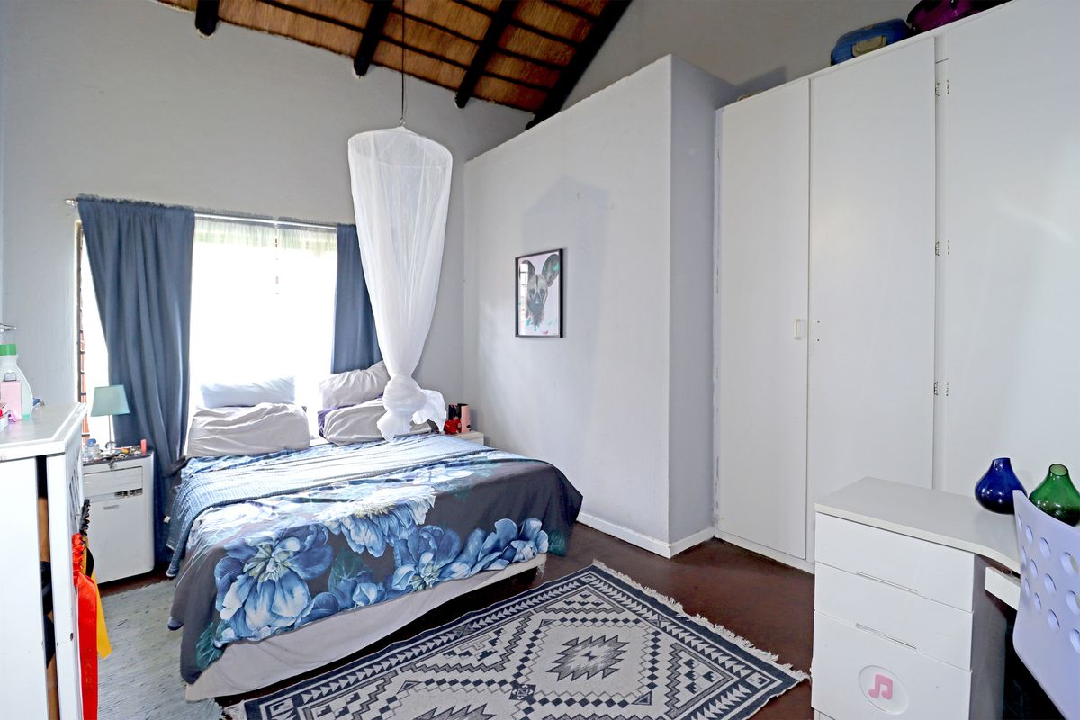 A bedroom featuring a high exposed thatch ceiling with timber rafters and built-in cupboards, offering a rustic aesthetic.