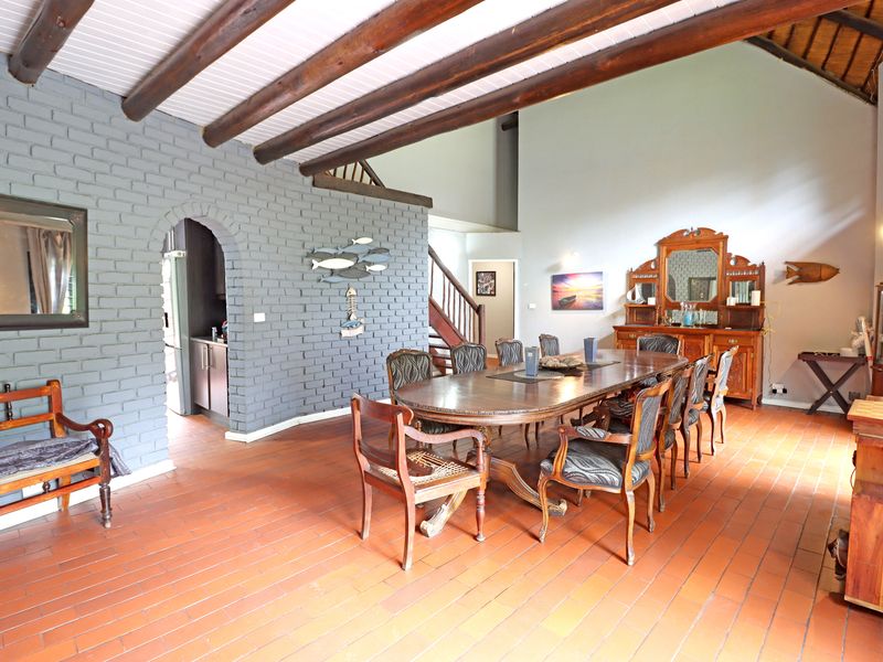 Spacious dining room featuring exposed timber ceiling beams, a grey brick feature wall, and terracotta tile flooring with an arched entrance to the kitchen.