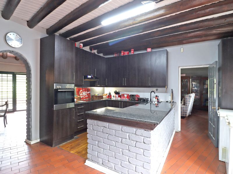 A functional kitchen featuring dark cabinetry, granite countertops, a brick breakfast bar, and exposed timber ceiling beams, complemented by terracotta floor tiles.