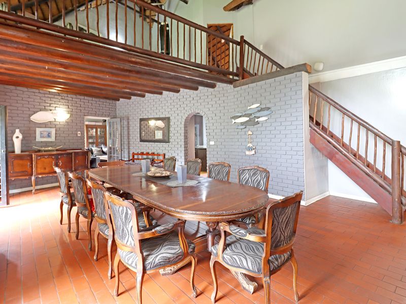 Spacious dining room featuring exposed timber beams, a mezzanine level with timber balustrade, terracotta flooring, and a distinctive painted brick feature wall.