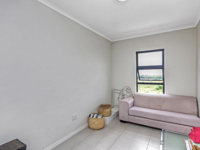 A living room featuring neutral tiled flooring, light-colored walls, and an aluminium-framed window providing natural light.