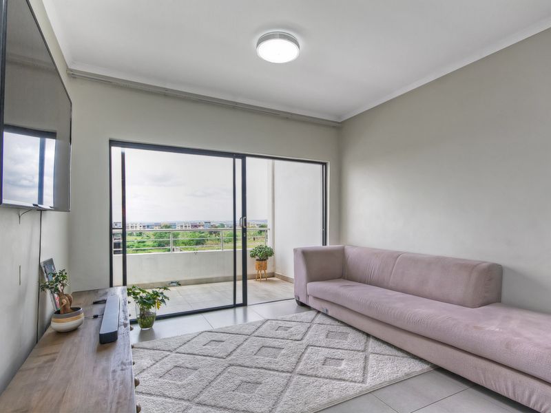 A bright living room featuring tiled flooring and a large sliding glass door that provides direct access to an outdoor balcony.
