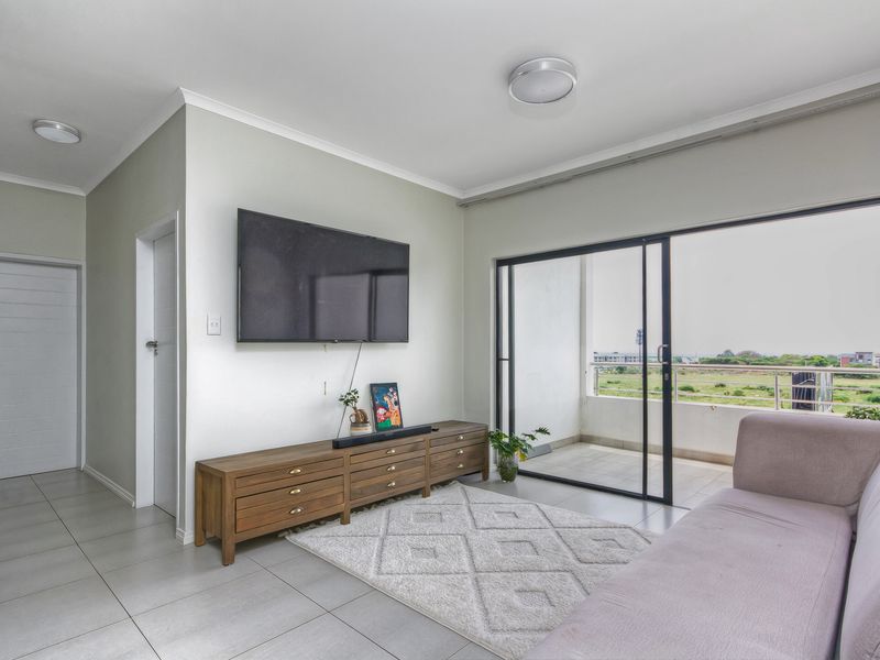 Bright living room featuring large sliding glass doors leading to a balcony, neutral tiled flooring, and clean wall finishes.