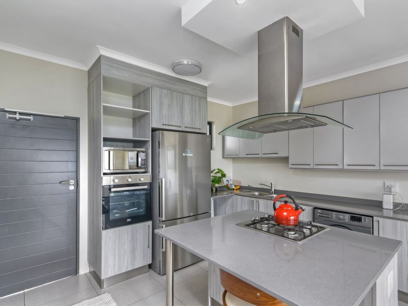 Modern kitchen featuring grey wood-grain cabinetry, stone countertops, a central island with a gas hob, and integrated stainless steel appliances.