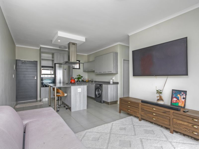 Modern open-plan living area featuring a contemporary kitchen with built-in cabinetry, integrated appliances, and a functional island, seamlessly connected to the lounge space.