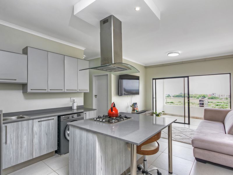 Modern open-plan kitchen and living area featuring a central island with gas hob, sleek cabinetry, and direct access to a private balcony.