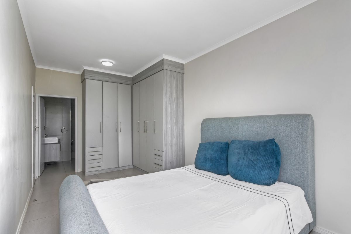 A well-maintained bedroom featuring modern built-in cupboards, neutral tiled flooring, and direct access to an en-suite bathroom.