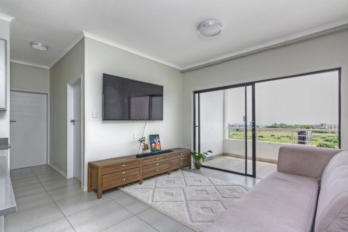Bright living room featuring large sliding glass doors leading to a balcony, neutral tiled flooring, and clean wall finishes.