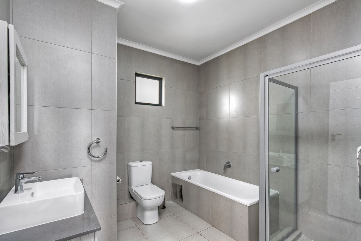 Modern bathroom featuring a built-in bathtub, separate glass shower enclosure, wall-mounted toilet, and a vanity basin with neutral grey wall and floor tiles.