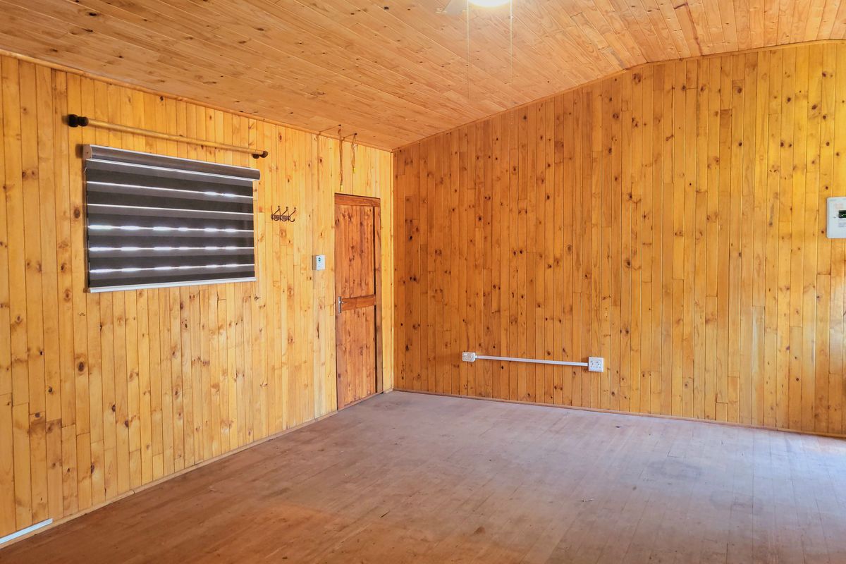 An empty living room featuring extensive timber wall paneling, a timber ceiling with a fan, and a single timber door.