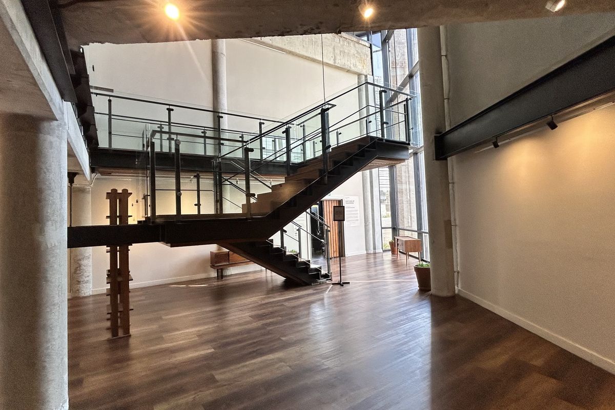 Spacious open-plan living area featuring a striking floating staircase with glass balustrades, hardwood flooring, and expansive floor-to-ceiling windows.