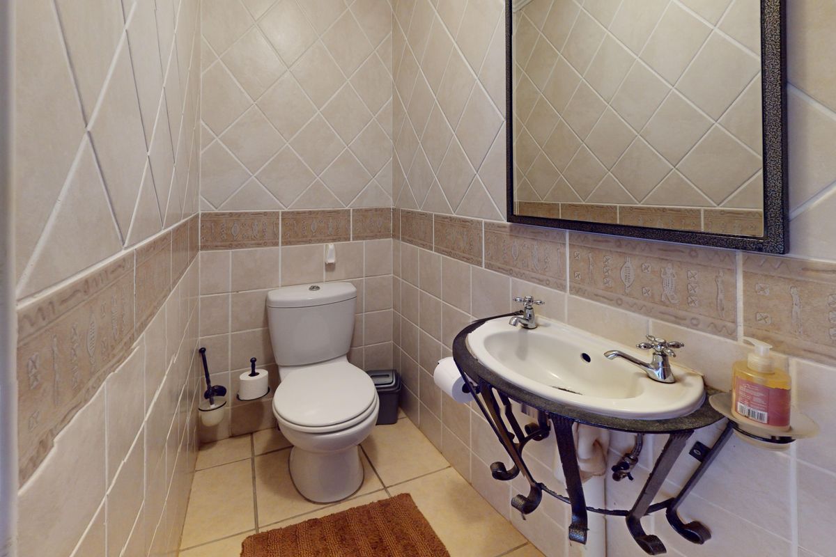 A compact guest bathroom featuring tiled walls with decorative accents, a wall-mounted basin with a wrought iron stand, and a standard toilet.