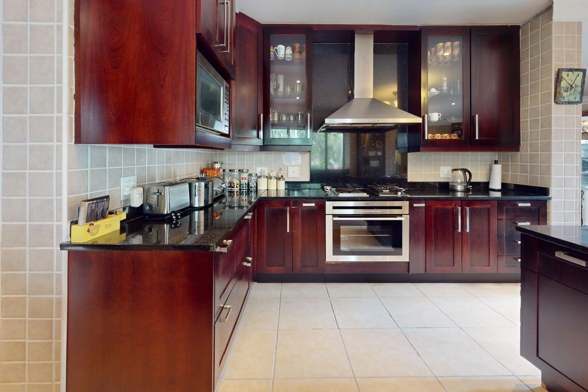 A well-appointed kitchen featuring dark wood cabinetry, granite countertops, integrated stainless steel appliances, and a tiled splashback.