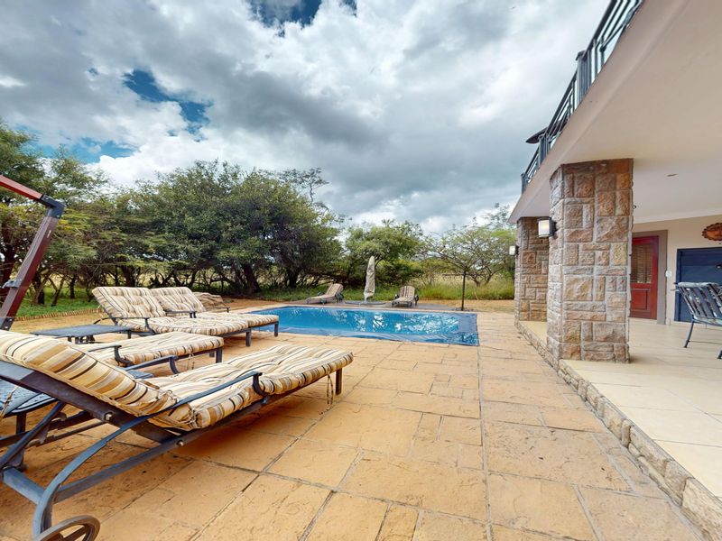 Outdoor pool area featuring a tiled patio, stone-clad structural pillars, and a swimming pool set against a natural landscape.